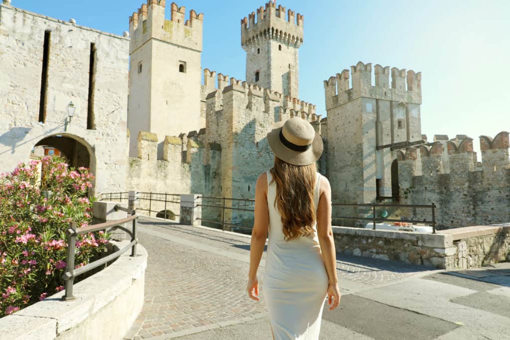 Travel in Italy. Back view of tourist woman walking in Sirmione towards the Scaligero Castle in lake garda